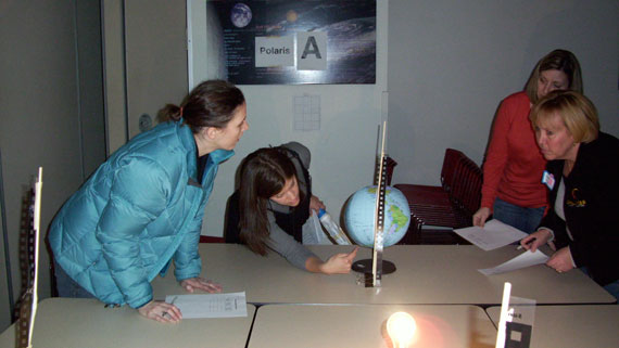 An Adler Planetarium educator and teacher workshop participants participate in a Reasons for the Seasons demonstration using an Earth globe and a bright light to represent the Sun.